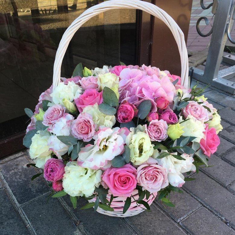 Wicker basket filled with pink and white flowers on a paved sidewalk