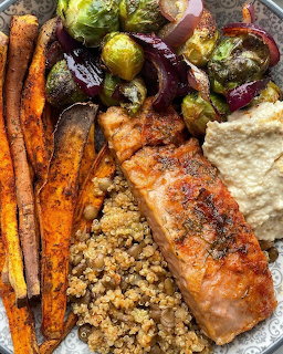 Roasted salmon with quinoa, carrots, Brussels sprouts, and hummus on a white plate