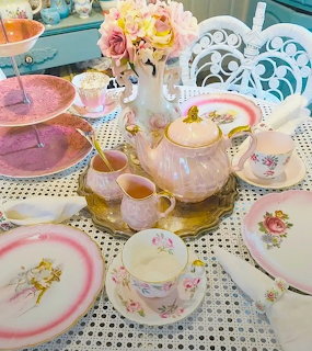 Elegant vintage tea party table with floral teapot, pastel cups, pink plates, and white ornate chairs