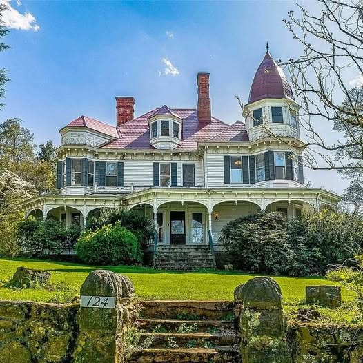 Large Victorian mansion with pink roof, turrets, and green shutters on sunny day with blue sky and lawn