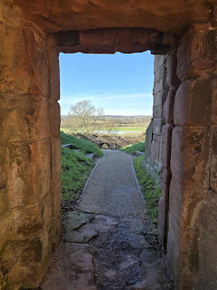 Stone archway opening to a path leading through countryside fields