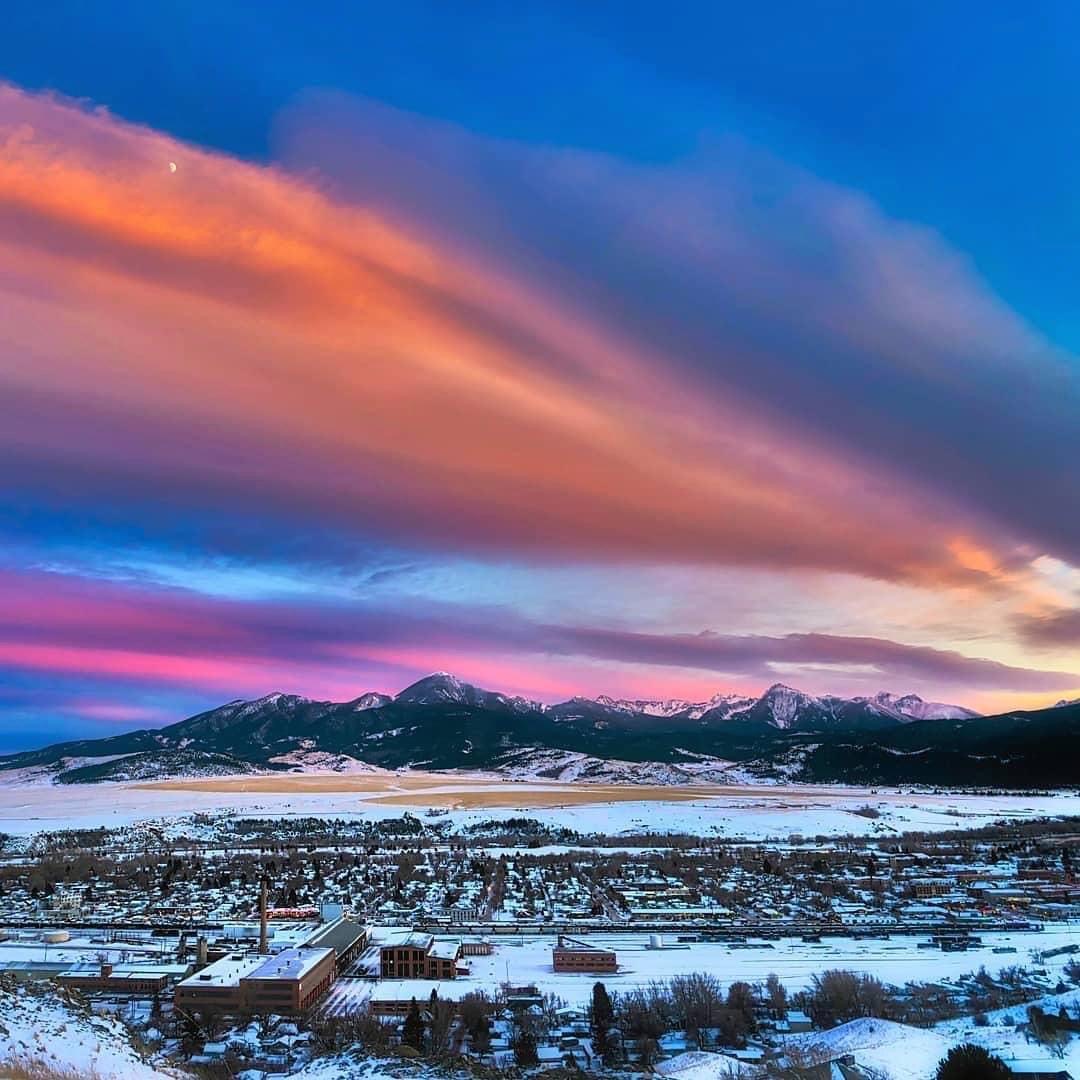 Snowy town below mountains at sunset with pink and blue clouds