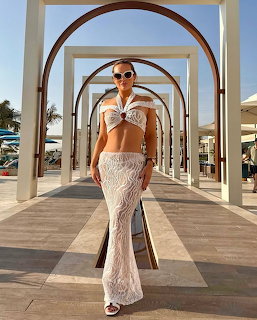 Woman in white crochet outfit under arched walkway at beach resort