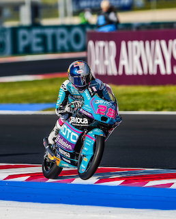 Moto3 rider in blue helmet on teal CFMoto racing bike leaning on track with Qatar Airways banner behind