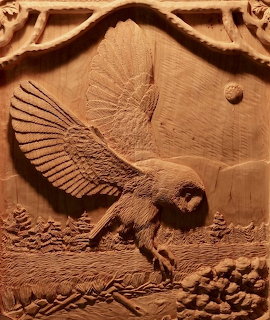 Wood relief carving of an owl landing with wings spread above a textured ground