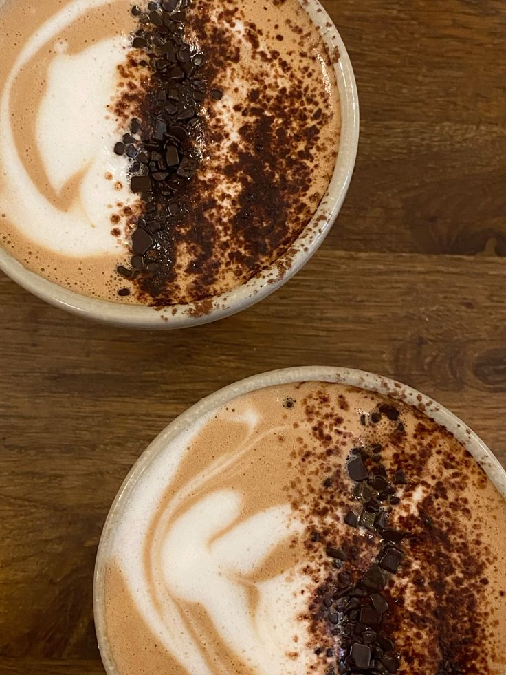 Two lattes with heart foam art and cocoa powder dusting on wood table