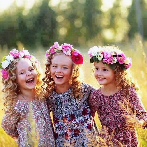 Three smiling girls wearing flower crowns and floral dresses in a sunny field