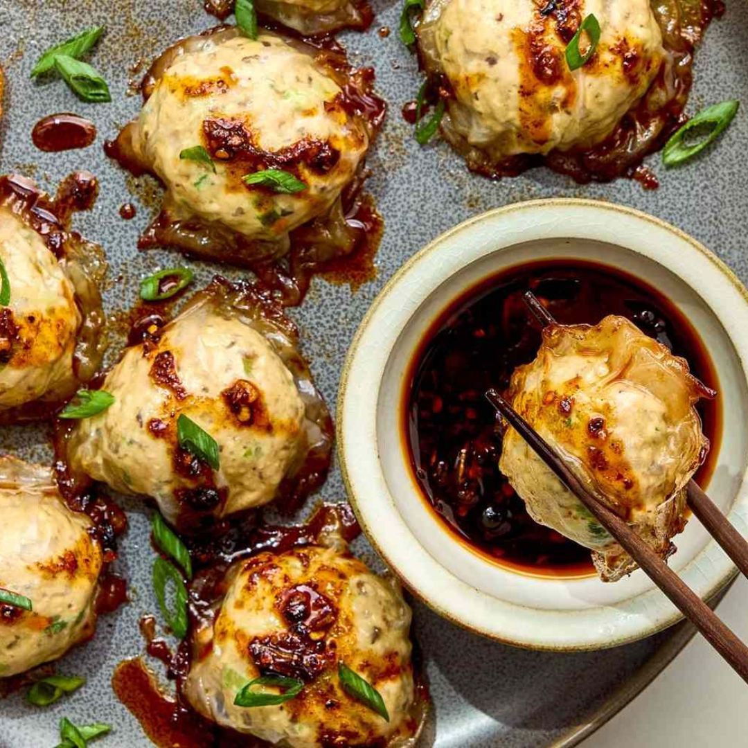 Golden pan-fried dumplings served with a bowl of dark dipping sauce