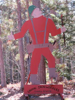 Red painted wooden cutout of an ironworker figure standing in a forest with a Union Ironworkers sign