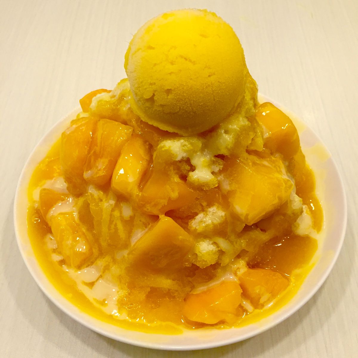 Bowl of mango shaved ice with mango pieces and a scoop of yellow ice cream on top