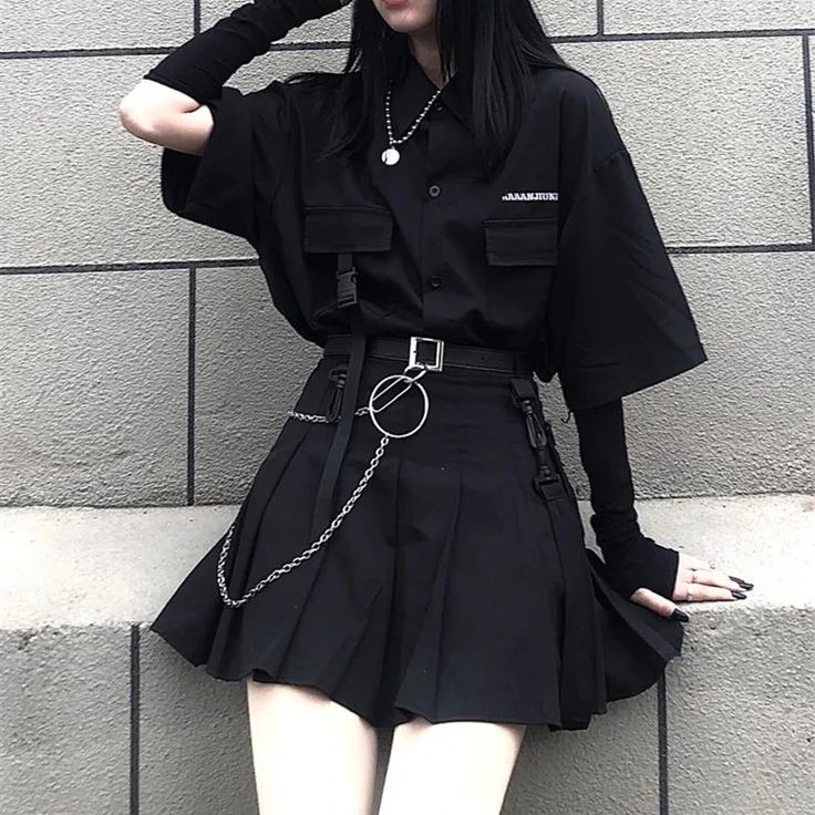 Woman in all-black gothic outfit with oversized shirt, pleated skirt, chain belt and silver necklace