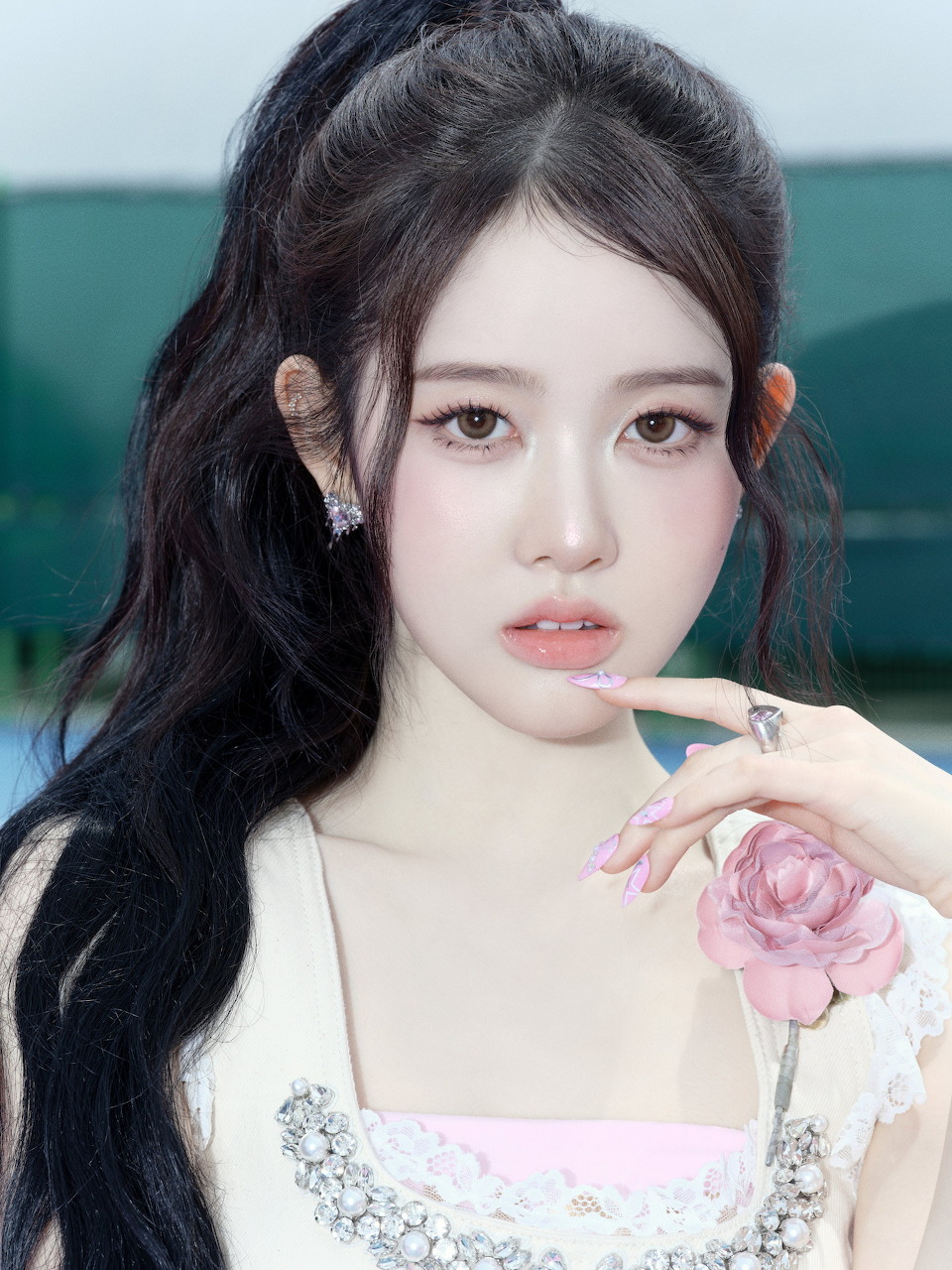 Portrait of young woman with long dark hair holding pink rose wearing white dress with jewelry accents