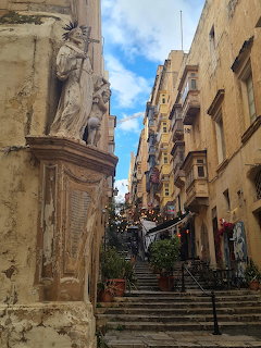 Narrow old stone street with steps, balconies, and a statue between historic buildings