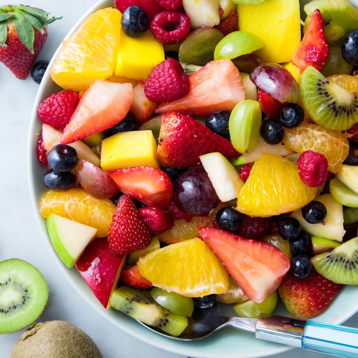 White bowl filled with colorful fresh fruit salad including strawberries, kiwi, oranges, and berries
