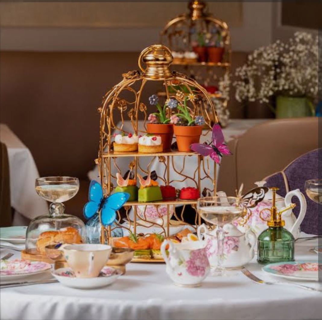 Ornate gold tiered stand displaying colorful desserts and treats with teapots and butterfly decorations on white table