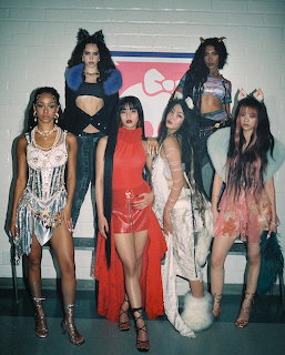 Five young women in stylish costumes posing together in front of a tiled wall