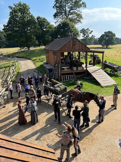 People and a horse outside a wooden barn in a sunny rural setting