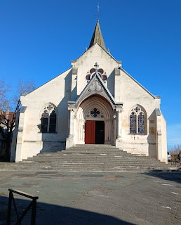 Stone church facade with steeple, arched red door and Gothic windows under blue sky