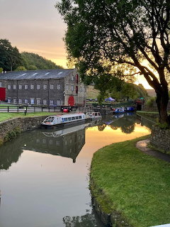 Narrowboats moored on a Yorkshire canal at sunset with a stone mill building and tree reflections on calm water.