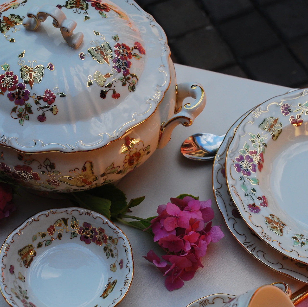 Elegant Zsolnay porcelain tea set with floral patterns and gold trim displayed with pink flowers