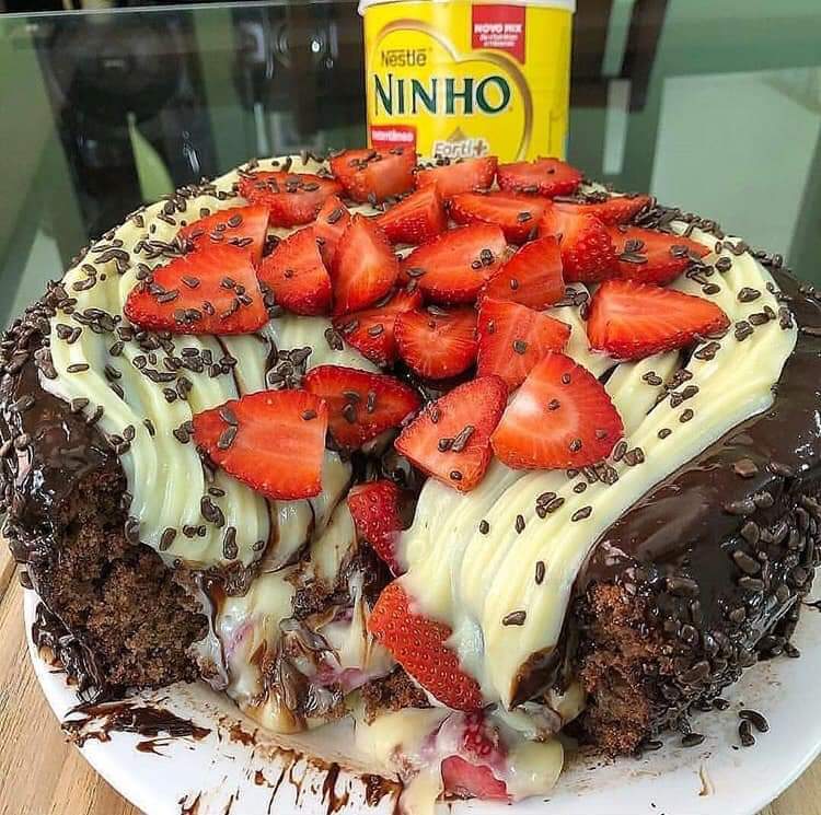 Chocolate cake topped with sliced strawberries, cream drizzle, and chocolate sprinkles