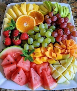 Colorful assorted fresh fruit platter with watermelon, mango, grapes, strawberries, oranges, and mint on a white plate