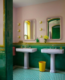 Retro bathroom with green tile walls and floor, pink upper walls, two white pedestal sinks, and yellow accents
