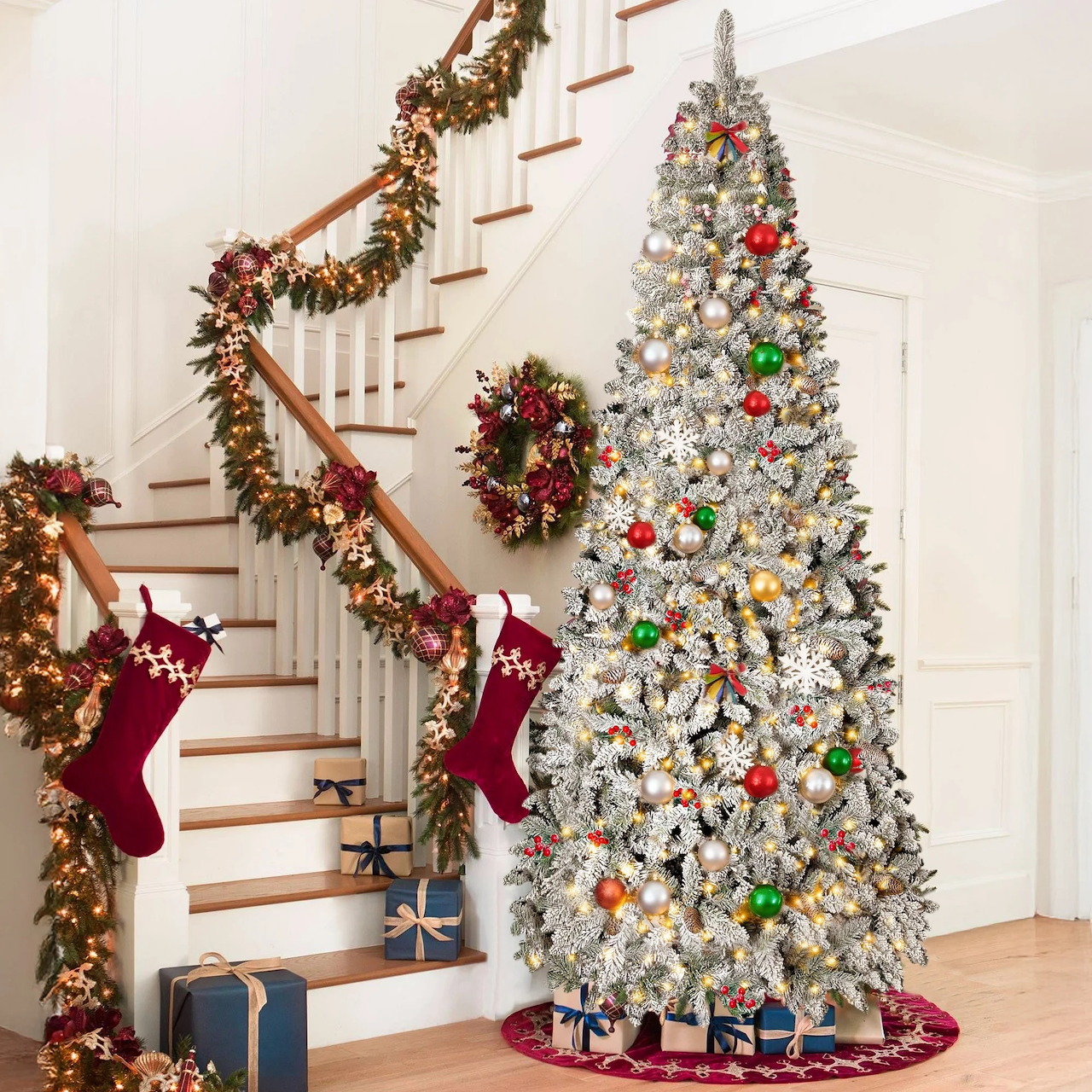 White Christmas tree with colorful ornaments beside staircase decorated with garland and red stockings
