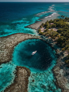 Aerial view of a blue hole in a coral reef with a small boat and tropical island