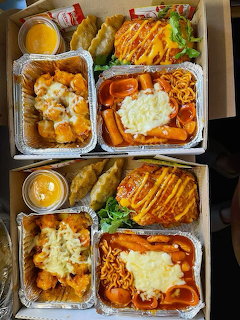 Korean takeout meal boxes with various dishes including teokbokki, fried foods, and grilled chicken in aluminum trays