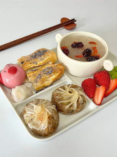 White tray with Korean food including dumplings, pastries, dessert soup, strawberries, and pink mochi