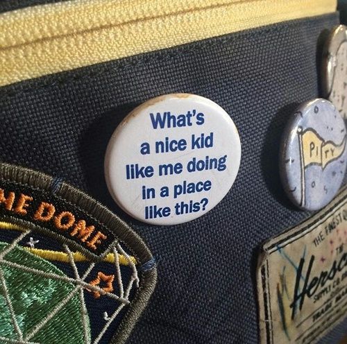 Close-up of pin badges on dark fabric, including a round badge with a quote