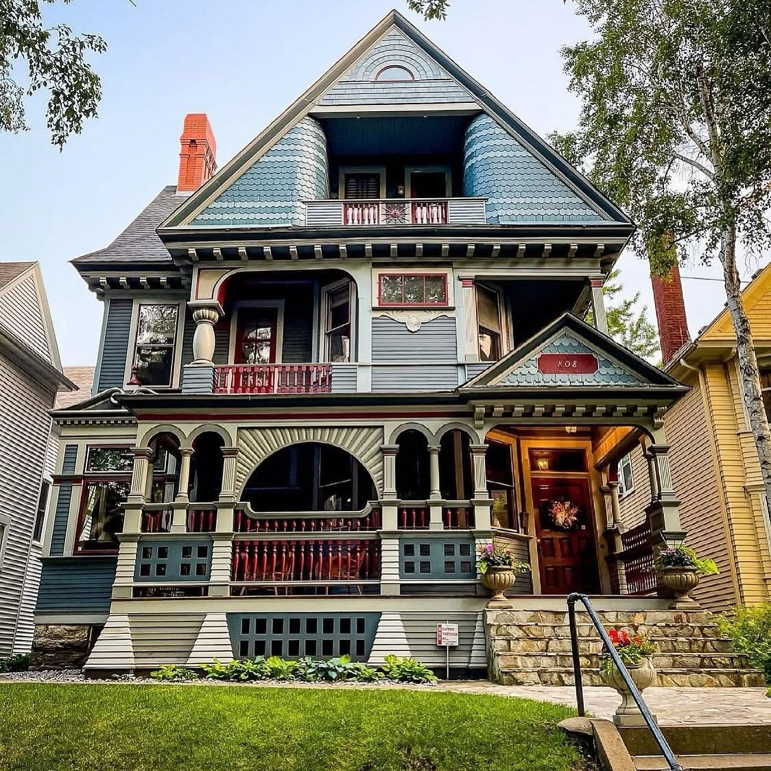 Victorian house with white siding, dark green trim, red brick chimney, and covered porches on multiple levels