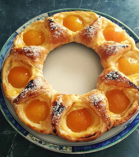 Ring-shaped apricot tart with puff pastry and powdered sugar on a blue decorative plate
