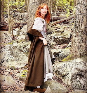 Woman with red hair in medieval dress standing in rocky forest