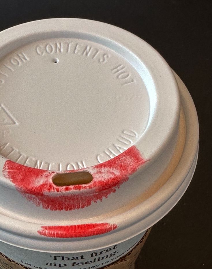 Takeaway coffee cup with white lid showing a red lipstick kiss mark