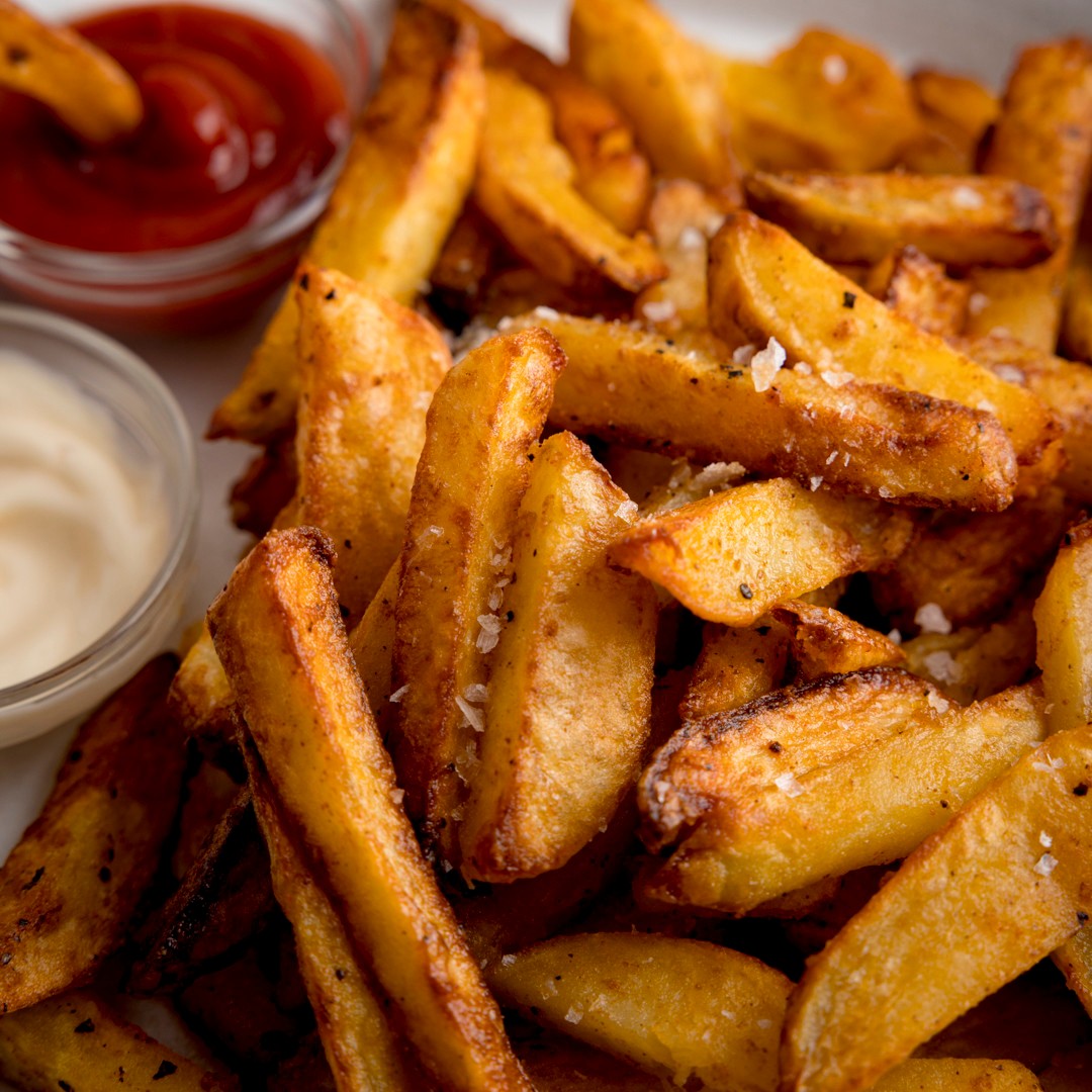 Close-up of crispy golden French fries with ketchup and creamy dipping sauce
