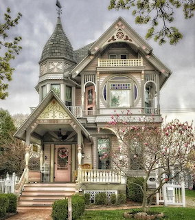 Ornate Victorian house with turret, decorative trim, porch railings, and flowering tree in front
