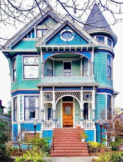Ornate blue Victorian house with turret, detailed trim, and front porch with brick stairs