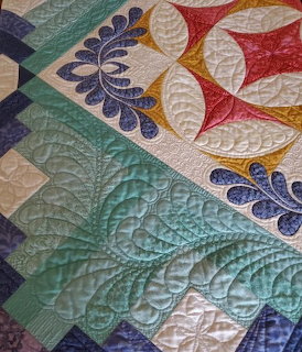 Detail of colorful quilt with embroidered feather patterns and decorative stitching in teal, white, red and blue fabrics