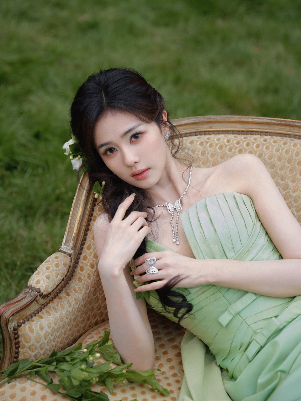Young Asian woman in a light green dress seated on an ornate chair outdoors with white flowers