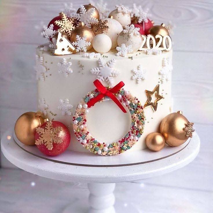 White Christmas cake with wreath decoration, gold baubles, and festive sweets on elegant cake stand