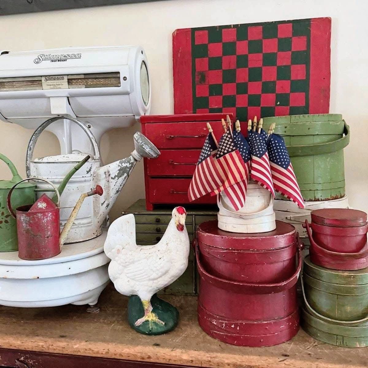 Vintage kitchen display with red and green metal containers, white pitcher, rooster figurine, and American flags