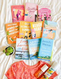 Collection of summer romance books displayed with coral dress on white bedding