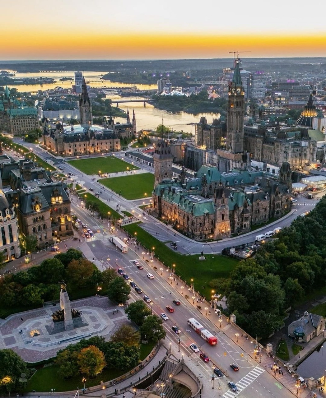 Aerial sunset view of Ottawa's Parliament Hill, gothic buildings, and city streets with the Ottawa River beyond