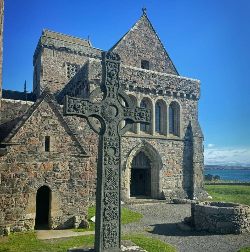 Old stone church with a Celtic cross in front beneath a bright blue sky