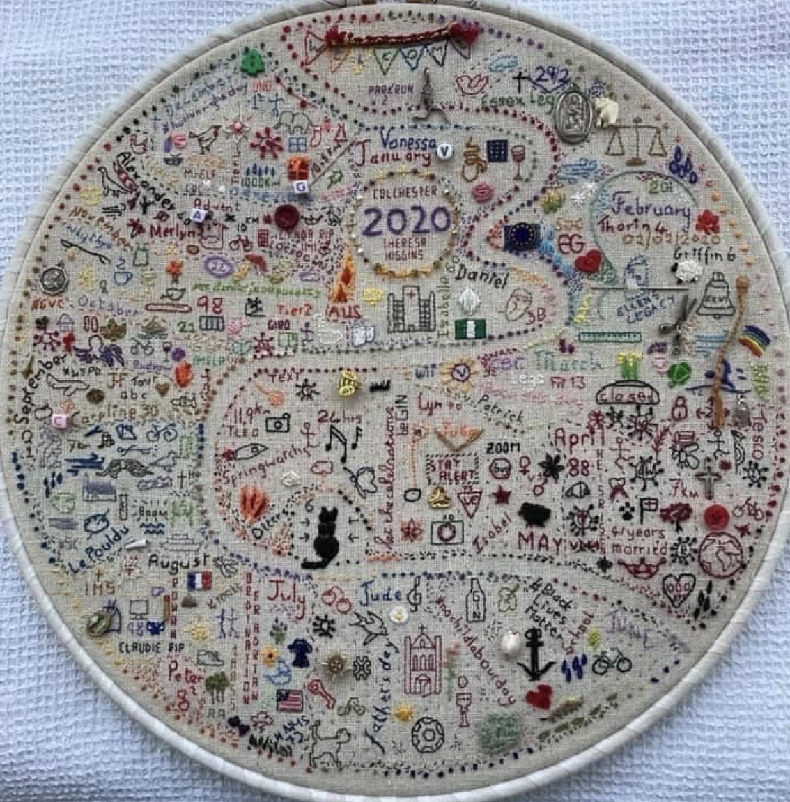 Circular embroidery hoop with a detailed stitched journal sampler filled with dates and tiny colorful motifs