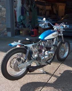 Vintage blue Triumph motorcycle with chrome engine parked outdoors in front of garage