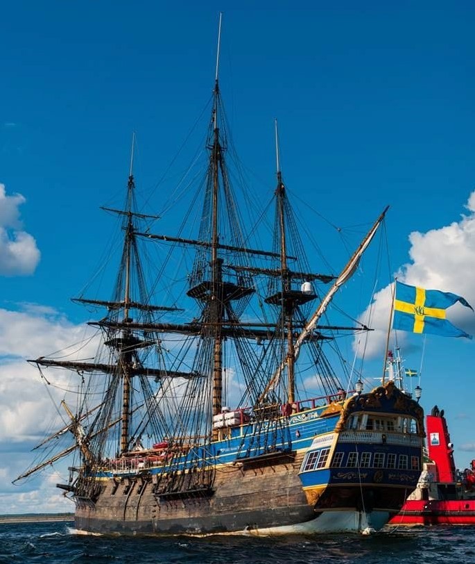 Historic tall ship Gotheborg on the water with a Swedish flag and red beacon under a blue sky
