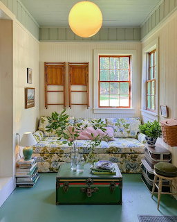 Vintage living room with floral couch, wood furniture, yellow pendant light, and pastel walls